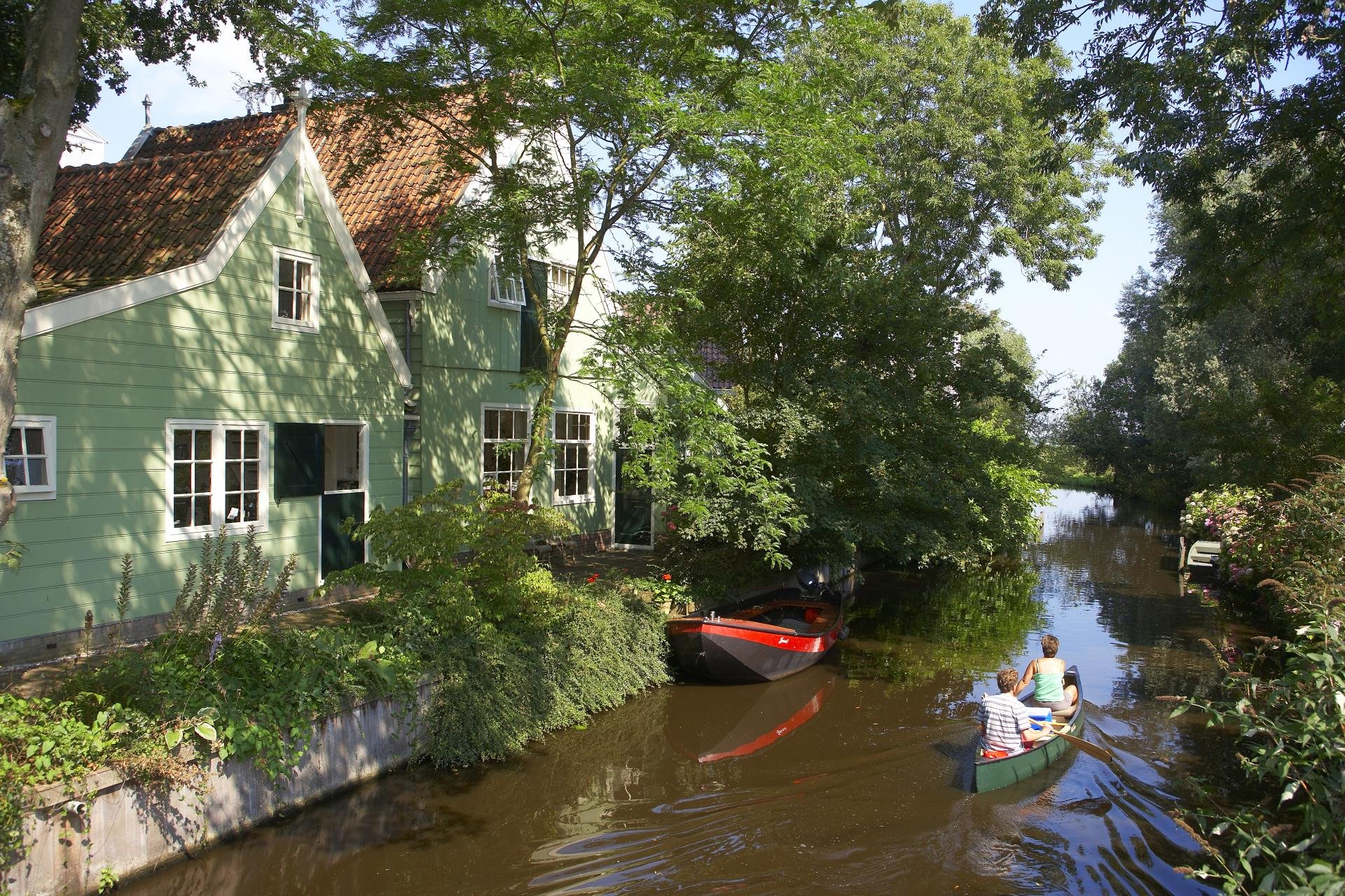 Zicht op monumentaal houten huis in Broek in Waterland vanaf de Kerkhofbrug met bootje in de Dee